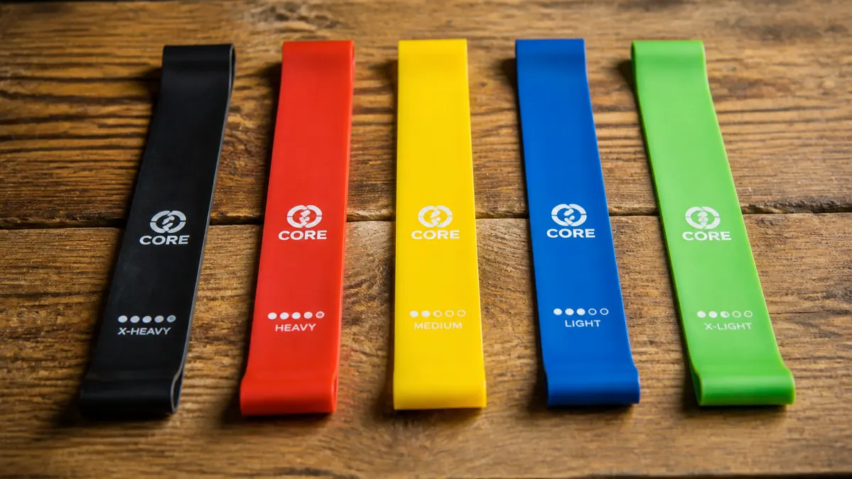 Five stacked resistance bands of increasing color and thickness lying in a neat row on a table