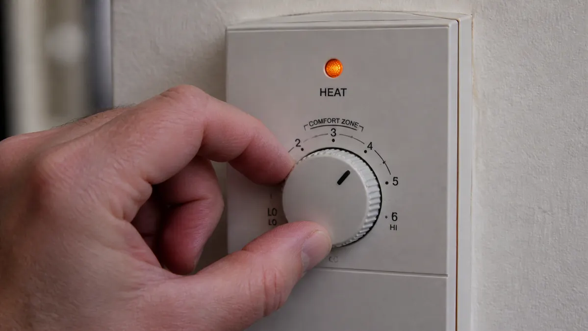 Close-up of a hand pressing the heat setting buttons on the pad's controller, with a red indicator light glowing